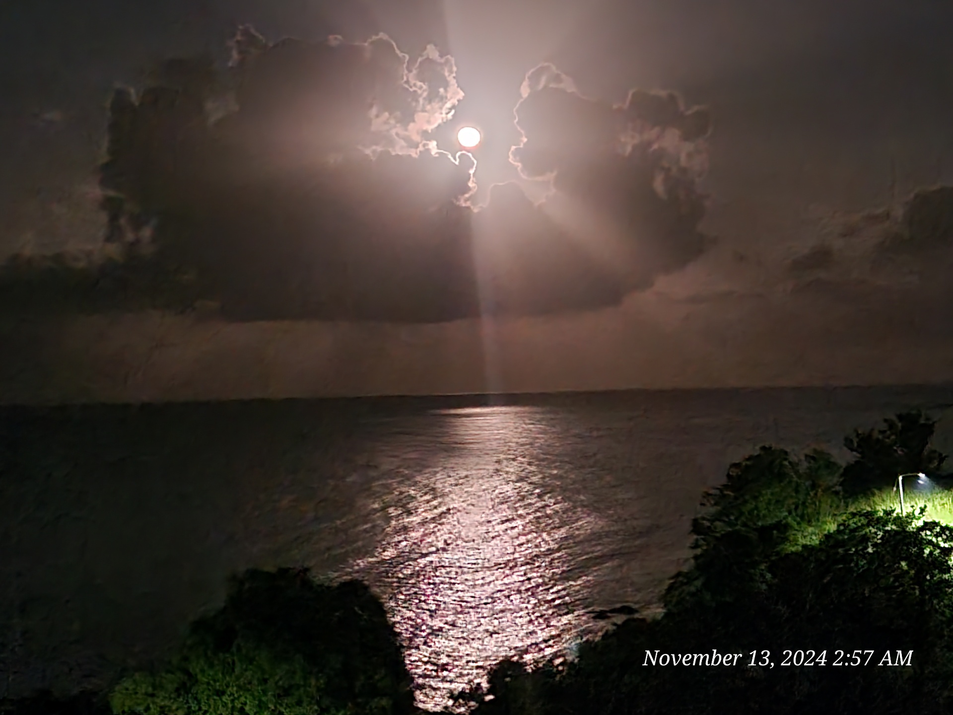 Moon shining through clouds over the sea with silver reflection on the water