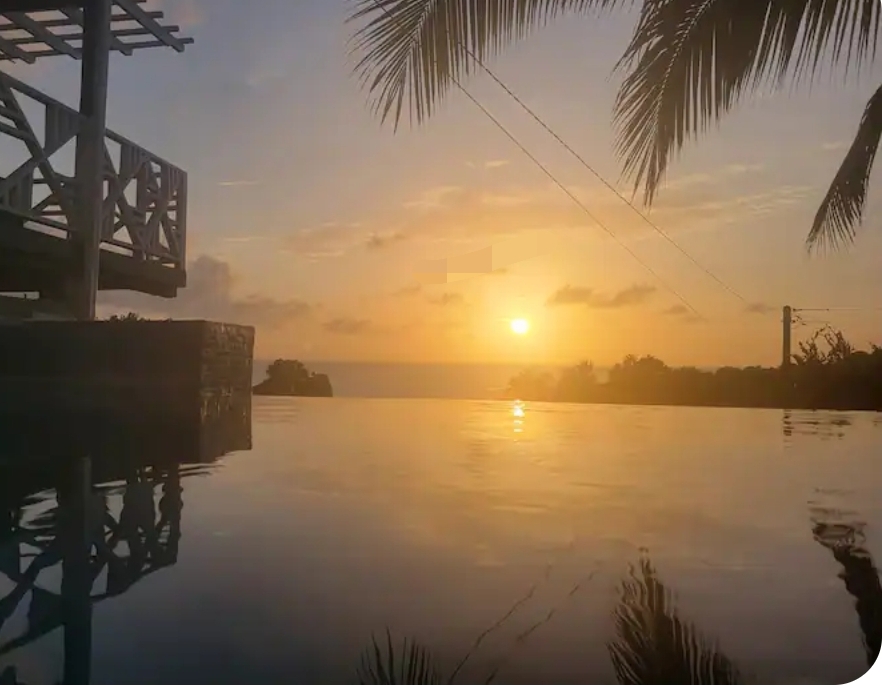 Sunset over the pool with palm fronds and sea horizon beyond